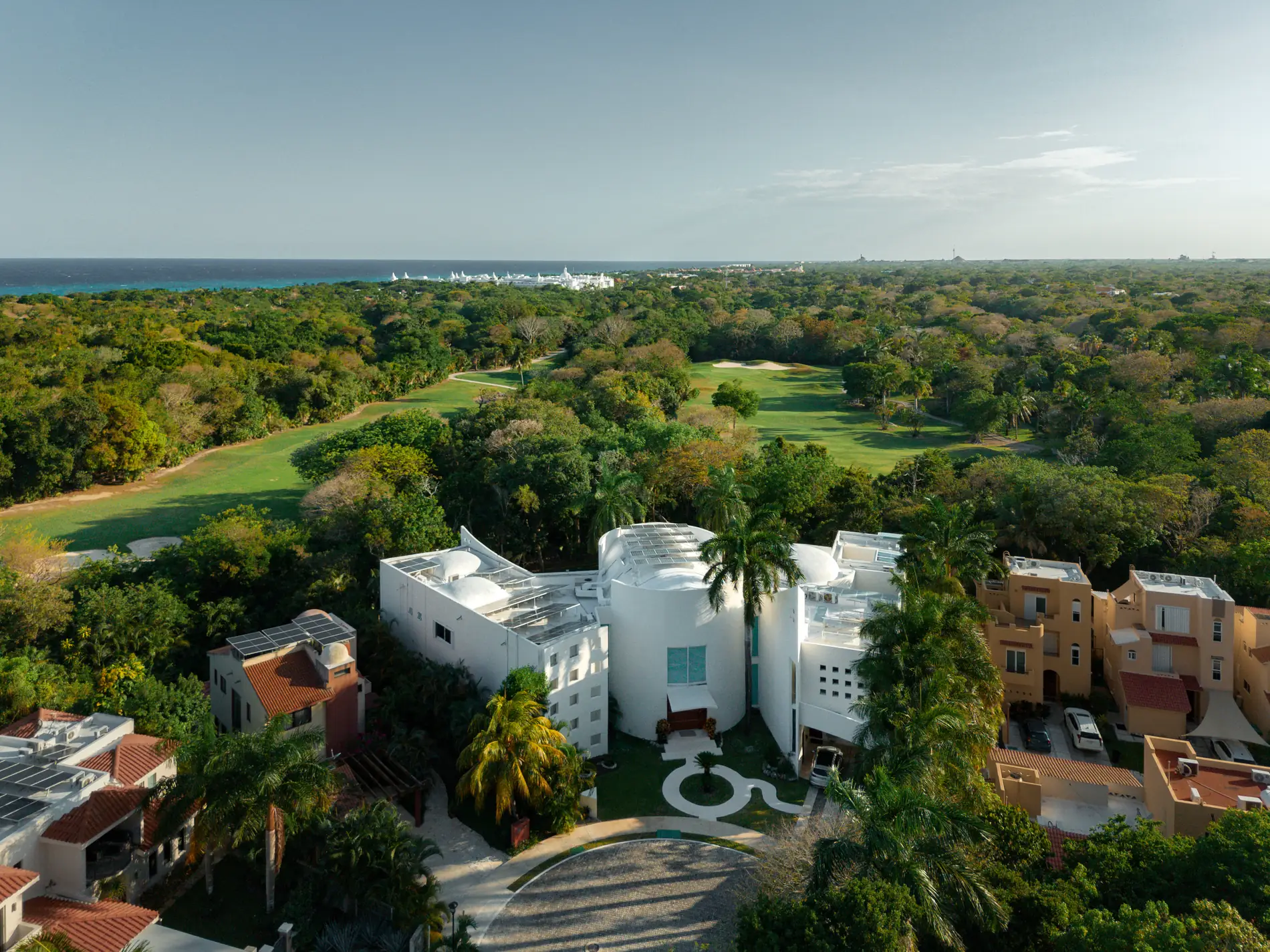 Aerial view of Villa Aqua among the jungle and golf course of Playacar, with the Caribbean Sea on the horizon